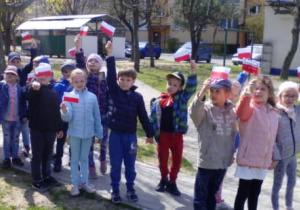 Dzieci na chodniku podczas spaceru z flagami biało-czerwonymi wykonanymi na zajęciu.